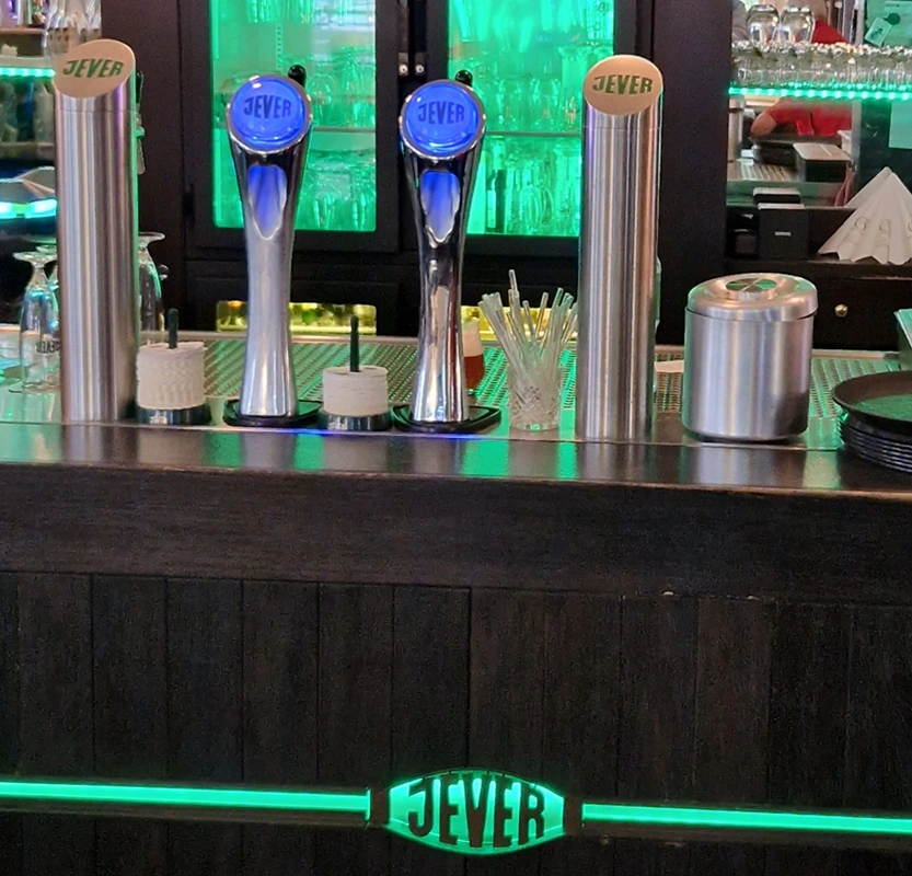 Mehrere Bierzapfanlagen mit Jever Logos stehen auf einer Theke. Im Hintergrund Gläser und grüne Beleuchtung.
