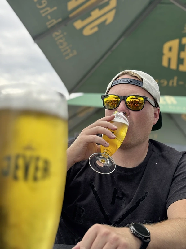 Ein Mann mit Sonnenbrille trinkt Bier aus einem Jever-Glas. Im Hintergrund ist ein grüner Sonnenschirm mit Jever Aufschrift.