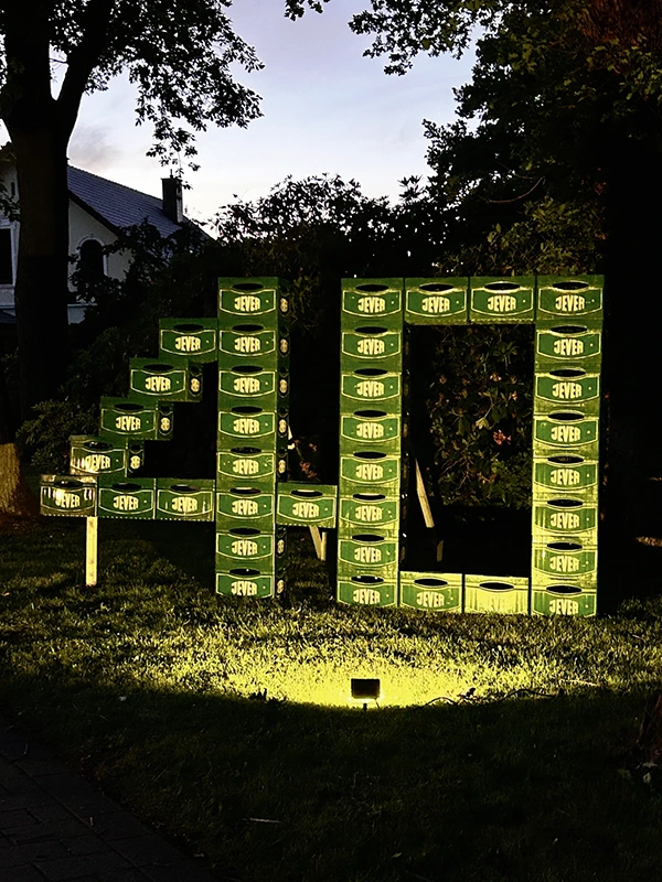 Mehrere Jever Kisten bilden eine große Zahl 40. Im Hintergrund sind Bäume und Häuser bei Abenddämmerung.