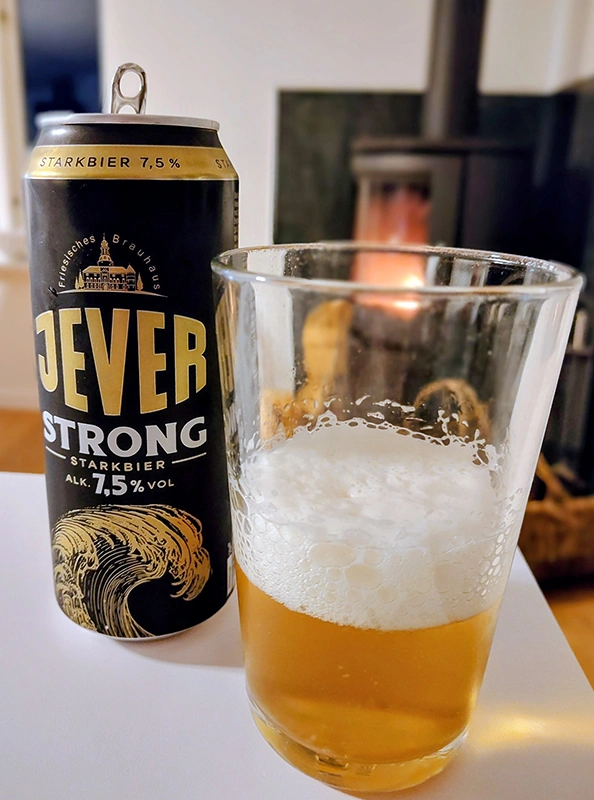 Jever Strong Bier in Glas eingeschenkt in Becher und Dose, stehen auf einem Tisch. Im Hintergrund ist ein Kamin.