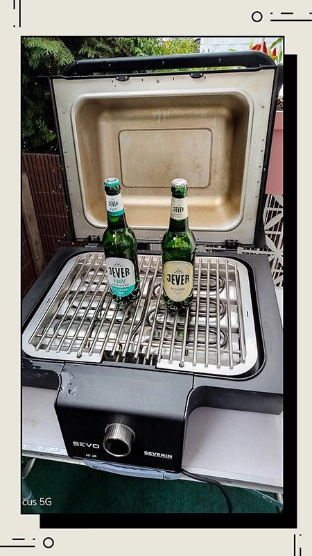 Zwei Jever Flaschen stehen in einem geöffneten, schwarzen Grill auf einem Metallrost.