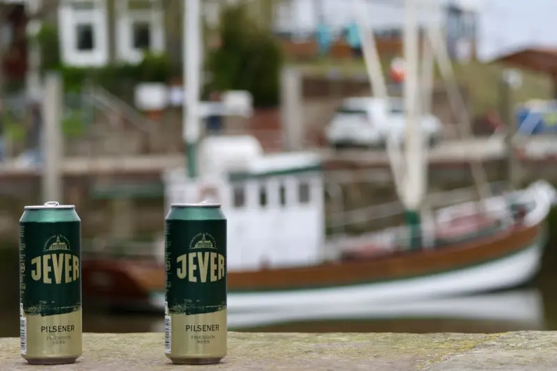 Zwei Jever-Bierflaschen stehen nebeneinander auf einer Mauer. Im Hintergrund befindet sich ein Boot.