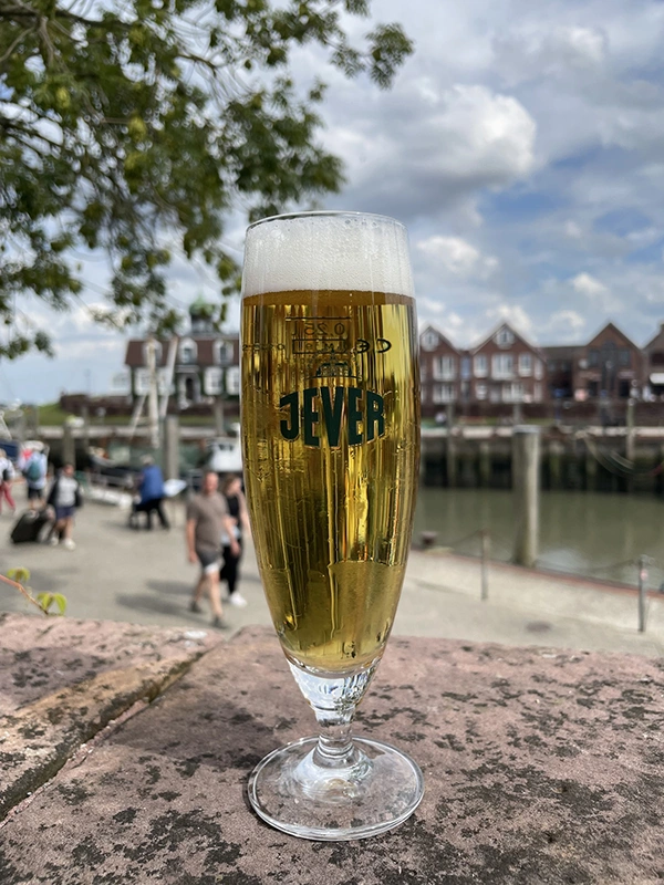 Ein Jever-Glas mit Bier darin steht auf einer Mauer an einem Hafen.