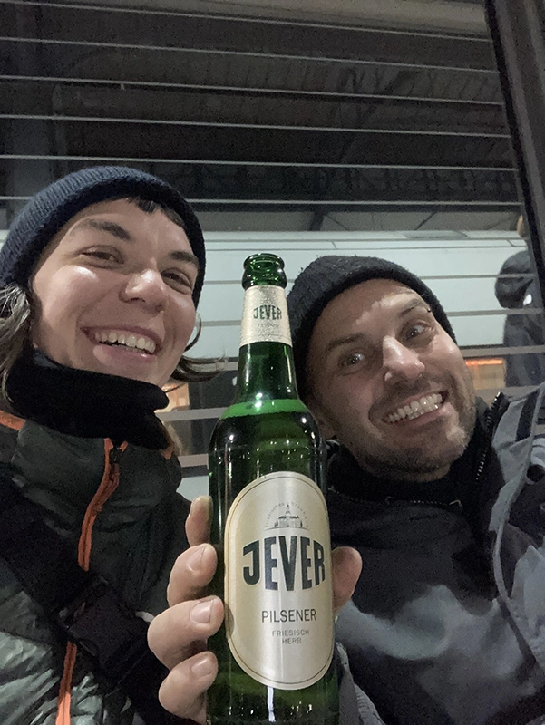 Ein lächelnder Mann hält eine Jever-Bierflasche vor sich. Links neben ihm sitzt eine Frau, die ebenfalls lächelt.