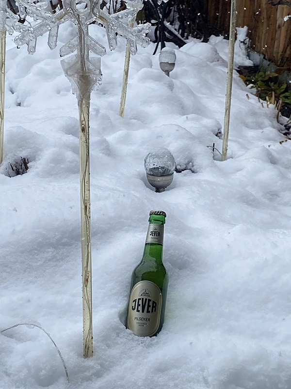 Eine Jever-Bierflasche liegt in einem Schneehaufen.