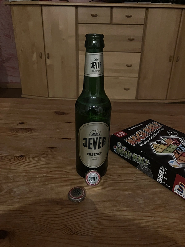 Eine Jever-Bierflasche steht auf einem Tisch. Rechts daneben liegt ein Würfelspiel.