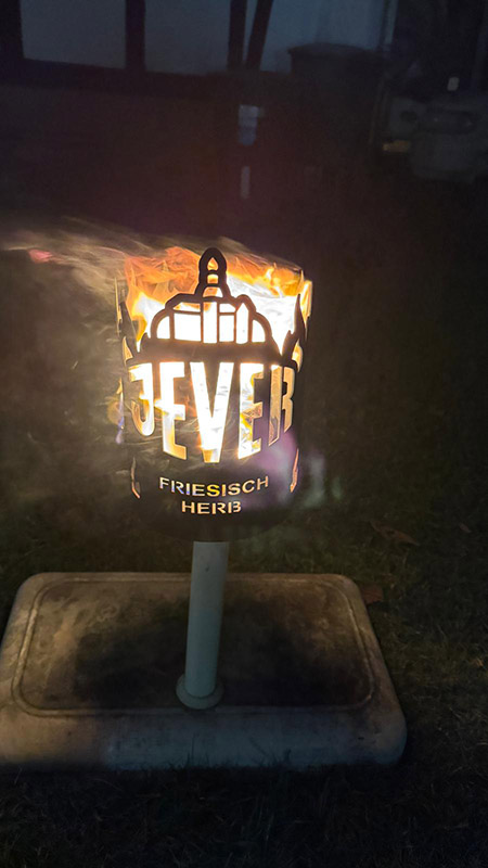 Auf einem Rasen steht eine brennende Fackel mit der Aufschrift Jever friesisch herb.