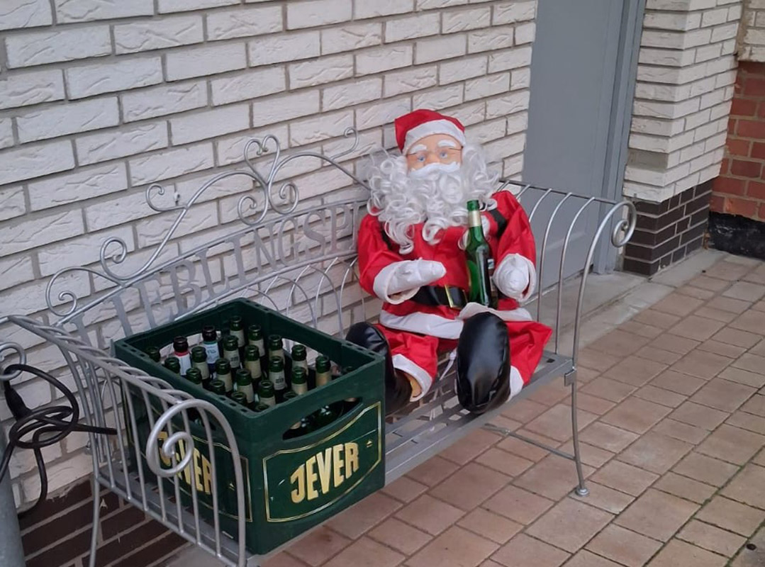 Auf einer Bank sitzt eine aufblasbare Weihnachtsmannpuppe mit einer Flasche auf dem Schoß, links daneben ist ein Jever-Bierkasten.