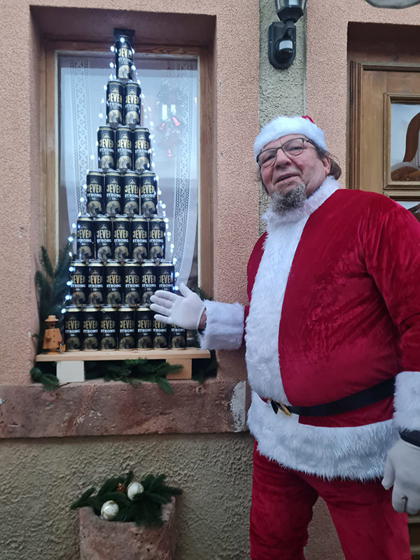 Ein Mann in einem Weihnachtsmannkostüm deutet mit seiner Hand auf eine Pyramide aus Jever-Bierflaschen.