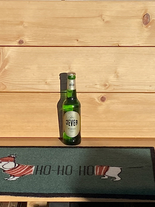 Eine Jever-Bierflasche steht hinter einer auf dem Boden liegenden Fußmatte, auf der ein Dackel abgebildet ist..