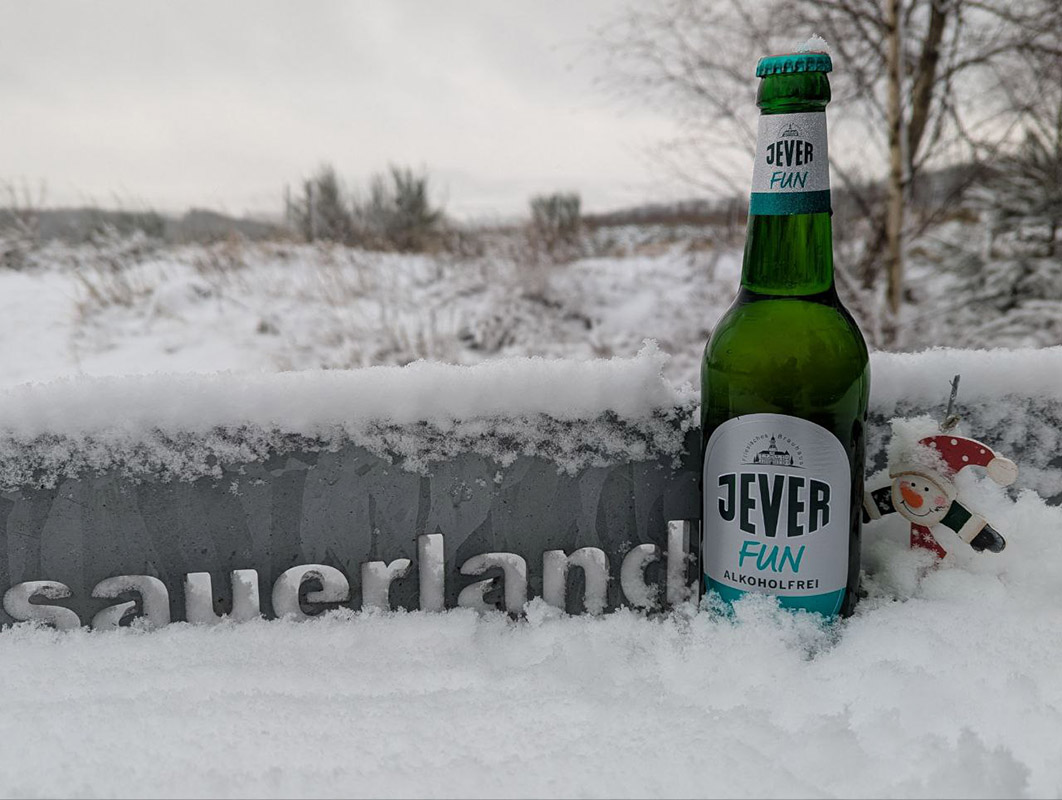 Eine Jever-Bierflasche steht vor einer Mauer mit Sauerland-Schriftzug im Schnee. Im Hintergrund ist eine verschneite Landschaft.