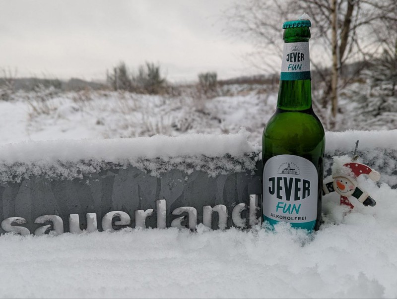 Eine Jever-Bierflasche steht vor einer Mauer mit Sauerland-Schriftzug im Schnee. Im Hintergrund ist eine verschneite Landschaft.