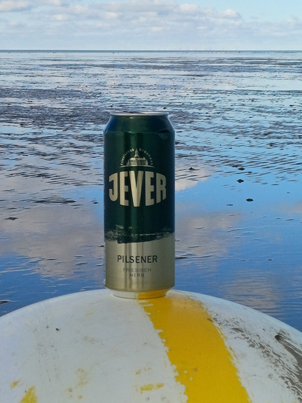 Eine Jever-Bierflasche steht auf einer Boje. Im Hintergrund ist Watt.