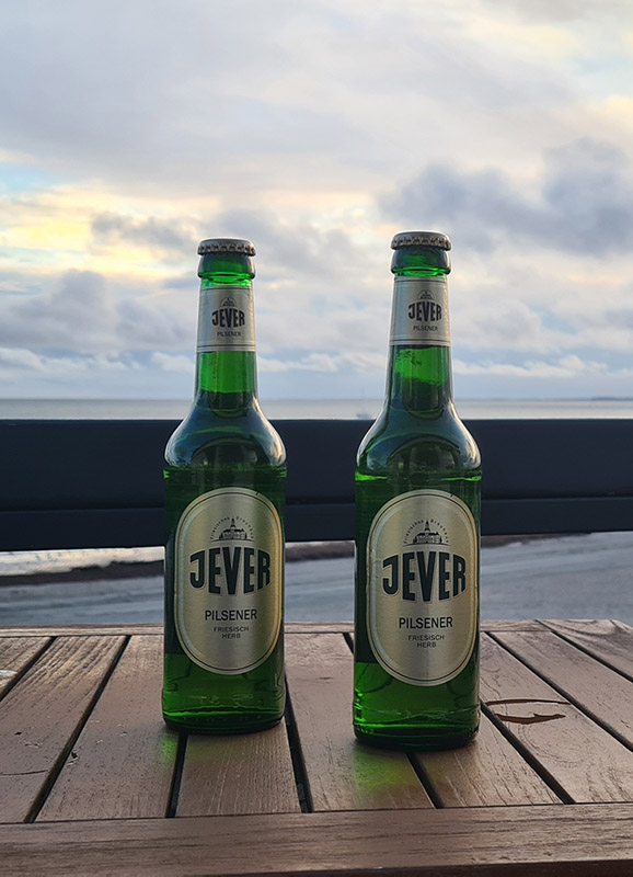 Zwei Jever-Bierflaschen stehen nebeneinander auf einem Holztisch.