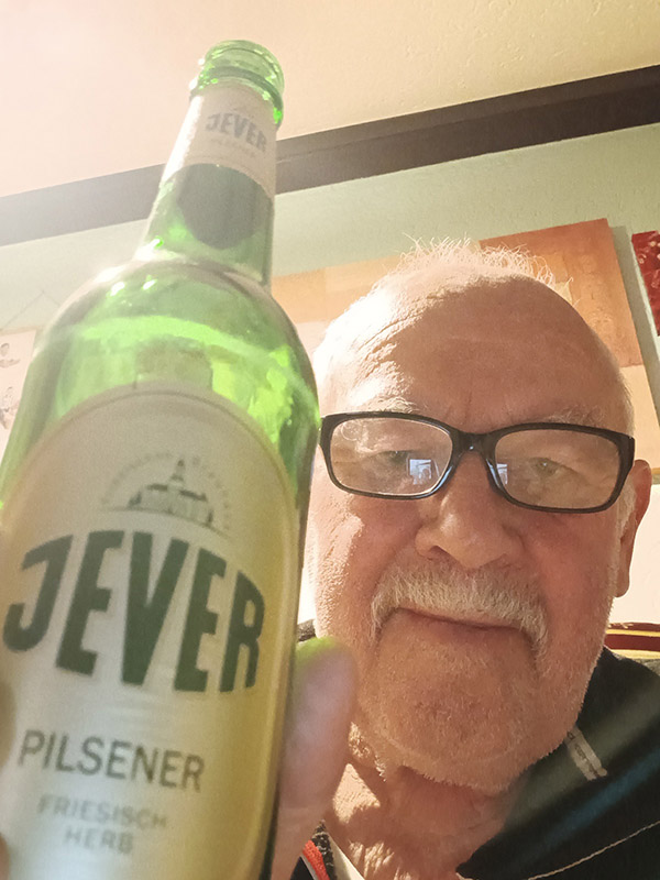 Ein Mann hält eine Jever-Bierflasche neben sein Gesicht.