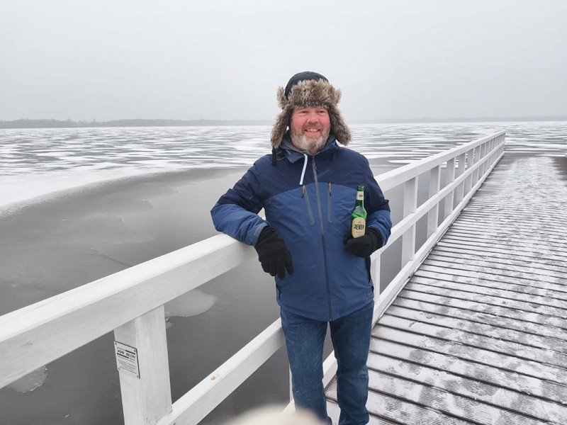 Ein Mann in Winterkleidung steht auf einem Steg und hält eine Jever-Bierflasche in der Hand.