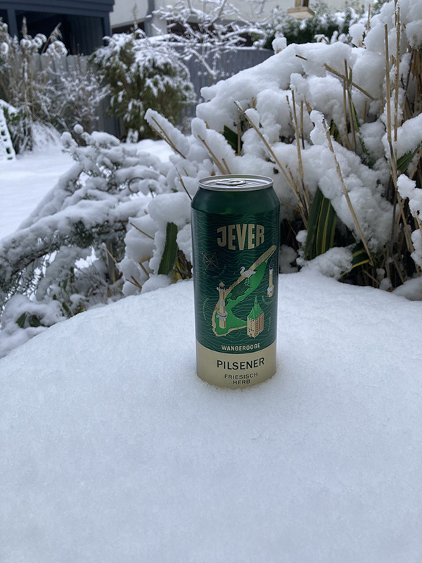 Eine Jever-Bierflasche steckt in einem Schneehaufen. Im Hintergrund ist ein verschneiter Garten.
