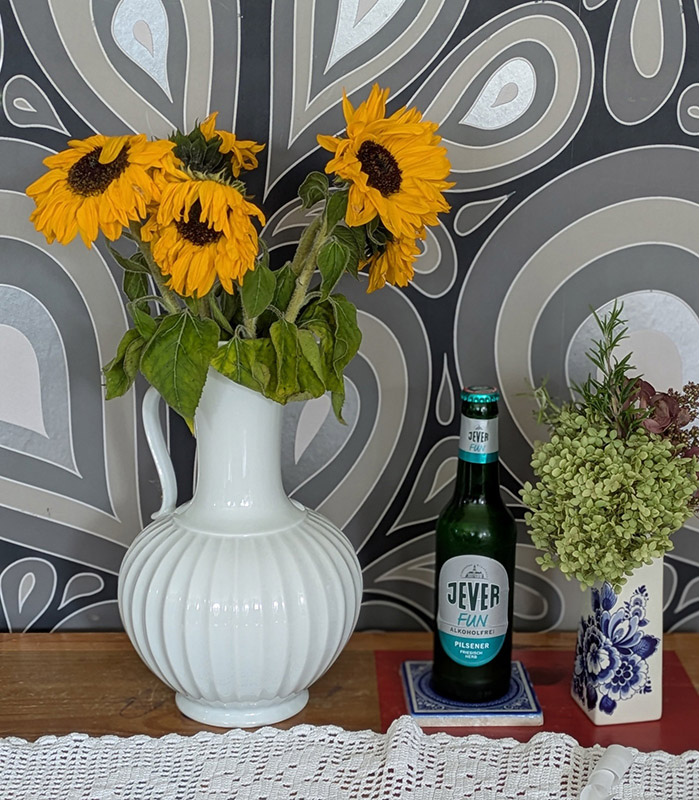 Eine Jever-Bierflasche steht zwischen zwei Vasen mit Blumen darin.