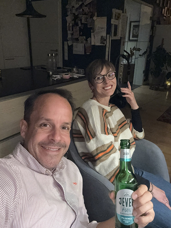 Ein lächelnder Mann hält eine Jever-Bierflasche hoch. Rechts neben ihm sitzt eine lächelnde Frau.