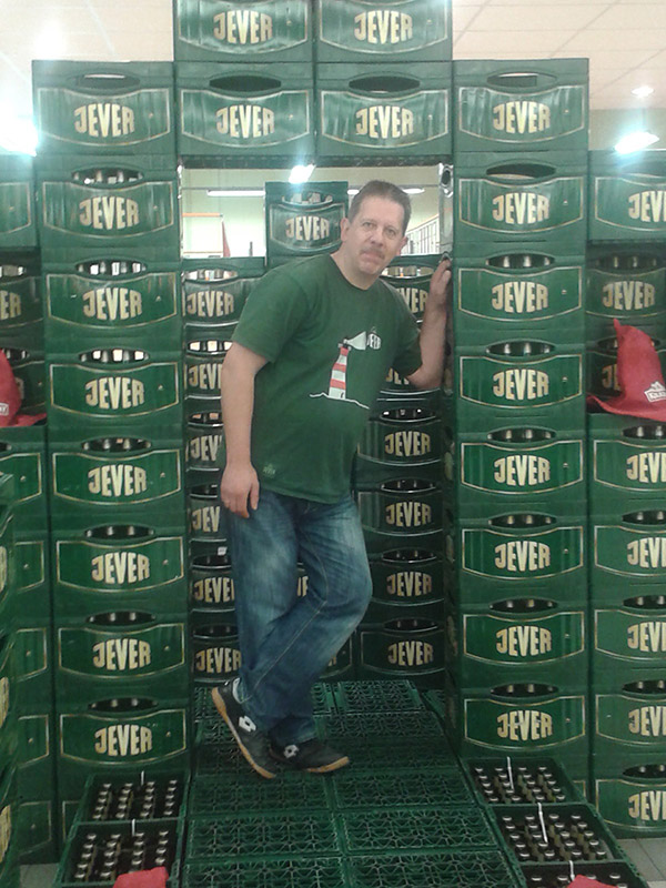 Ein Mann steht inmitten von aufeinander gestapelten Jever-Bierkästen.