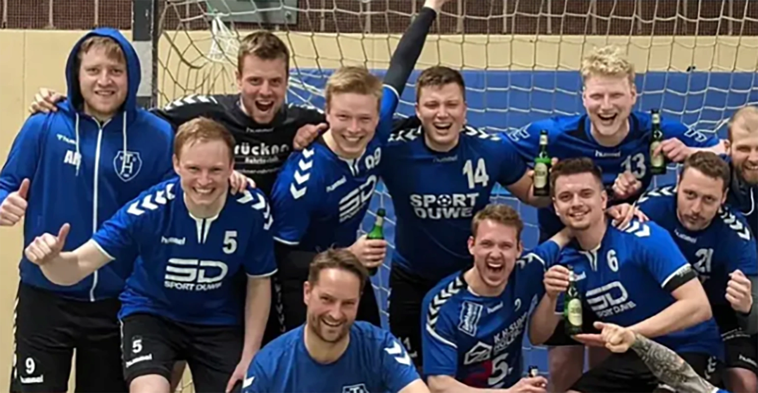 Eine Gruppe von Handballspielern in blauen Trikots jubelt freudig vor einem Tor mit Jever Flaschen in der Hand.