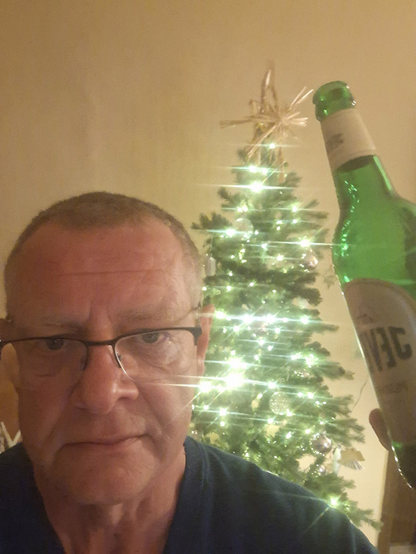 Ein Mann hält eine Jever-Bierflasche neben sein Gesicht. Hinter ihm steht ein dekorierter Weihnachtsbaum.