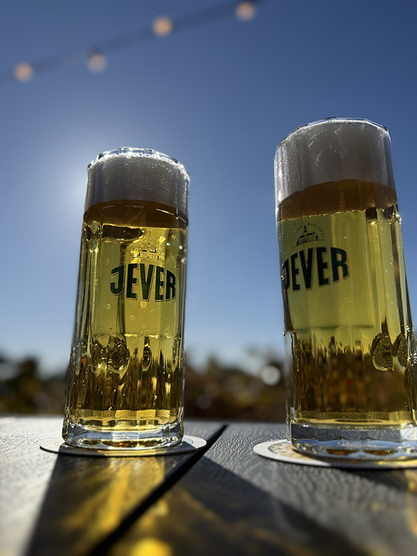 Zwei Jever-Gläser mit Bier darin stehen nebeneinander auf einem Tisch.