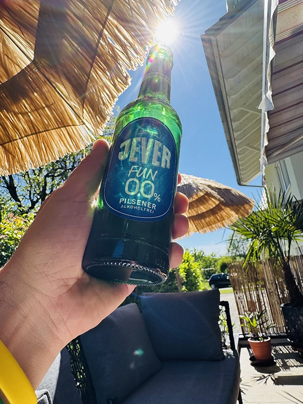 Eine Person hält eine Flasche alkoholfreies Jever Pilsener in die Sonne.