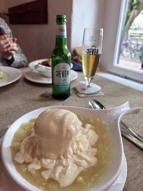 Ein Dessert aus Vanillesoße und Birnen auf einem Tisch. Im Hintergrund eine Flasche und ein Glas mit Jever Fun. 