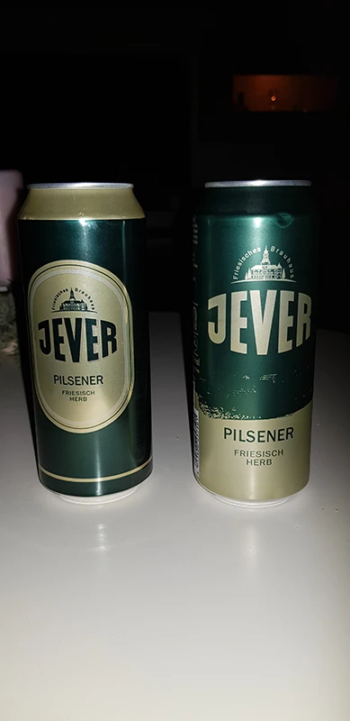 Zwei grüne Dosen Jever Pilsener stehen nebeneinander auf einem Tisch, eine mit ovalem Logo, die andere ohne Rahmen.
