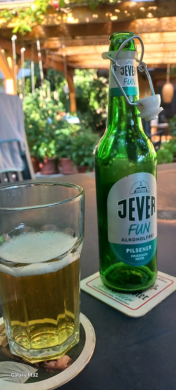 Glas mit hellem Bier neben einer Flasche Jever Fun Alkoholfrei auf einem Tisch im Außenbereich.