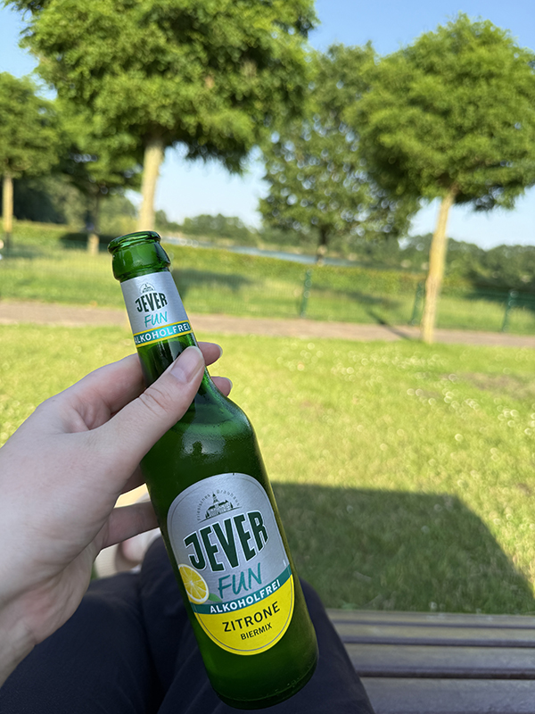 Im Vordergrund eine Flasche Jever Fun Zitrone, alkoholfrei. Dahinter eine sonnige Parklandschaft mit Bäumen und grünem Gras.