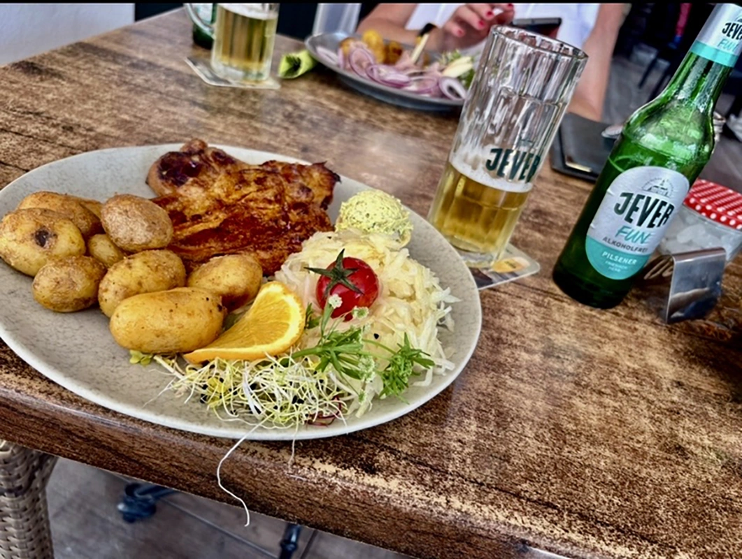 Ein Teller mit Bratkartoffeln, gegrilltem Fleisch und Salat. Daneben ein Glas und eine Flasche Jever Bier.
