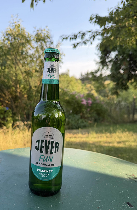 Eine Flasche Jever FUN steht auf einem grünen Tisch im Garten. Die Umgebung ist grün und sommerlich.