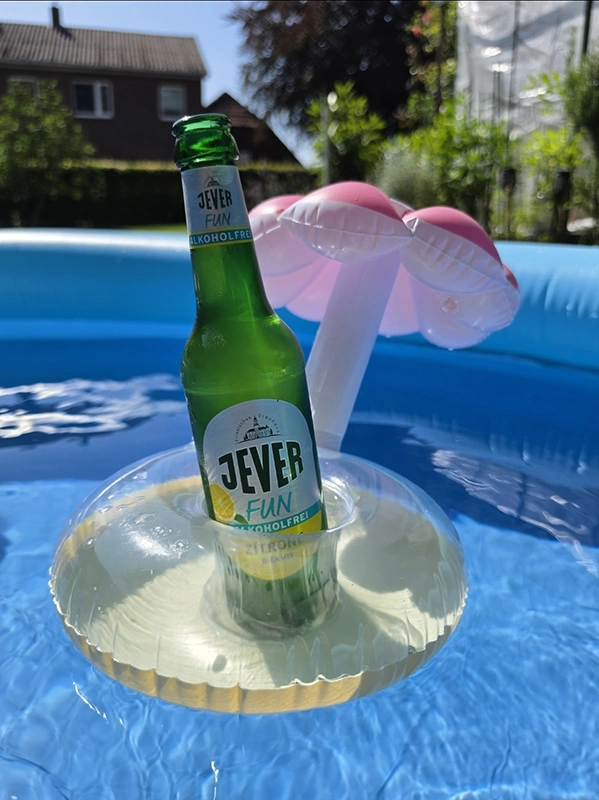 Eine Flasche alkoholfreies Bier schwimmt in einem aufblasbaren Halter im Pool. Im Hintergrund ein Haus und Bäume. 