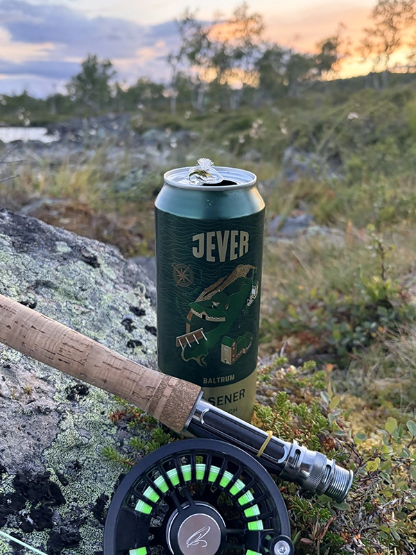 Grüne Jever Bierdose mit Angelrute auf moosbewachsenem Felsen. Abendhimmel und Bäume im Hintergrund.