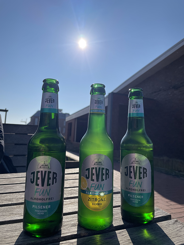Drei Flaschen Jever Fun alkoholfrei auf einem Tisch im Freien. Die Sonne scheint hell am klaren blauen Himmel. 