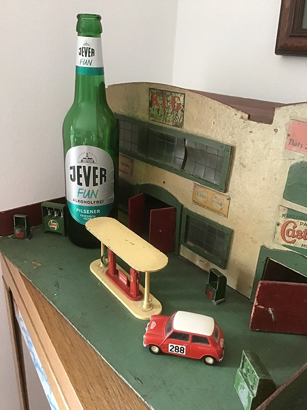 Eine Jever Fun Flasche steht neben einem Modell einer Tankstelle mit einem kleinen roten Spielzeugauto. 