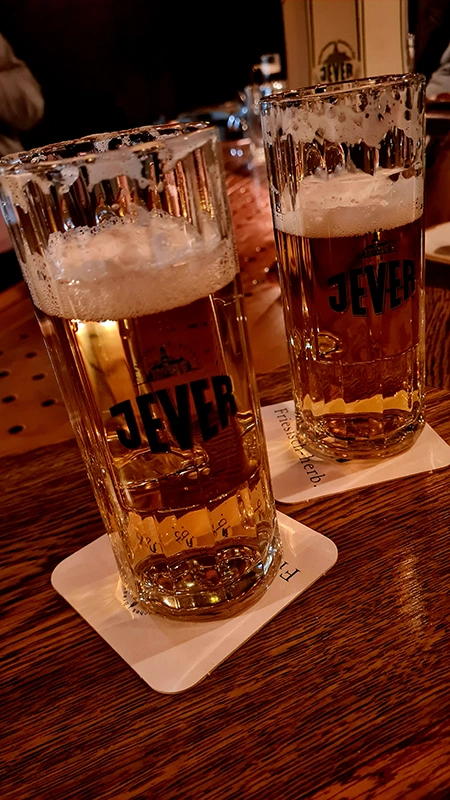 Zwei mit Jever Bier gefüllte Gläser stehen auf Untersetzern auf einem Holztisch.