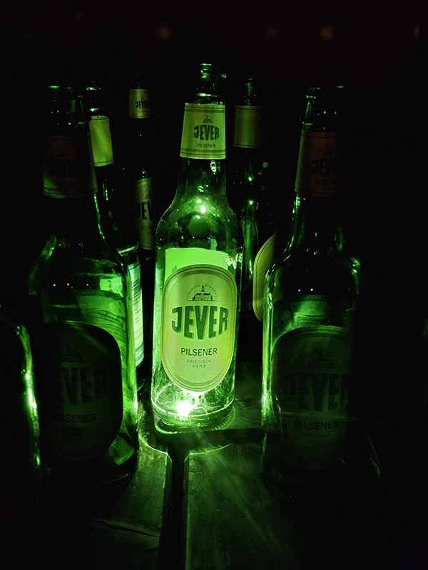 Mehrere Jever Flaschen stehen im Dunkeln. Eine Flasche in der Mitte wird von grünem Licht beleuchtet.