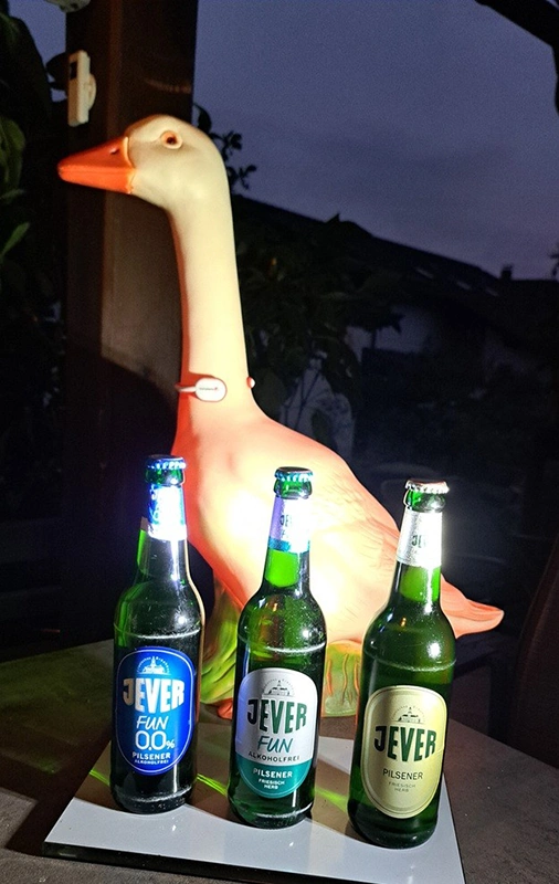 Drei verschiedene Jever Flaschen stehen vor einer beleuchteten Gänsefigur in dunkler Umgebung.
