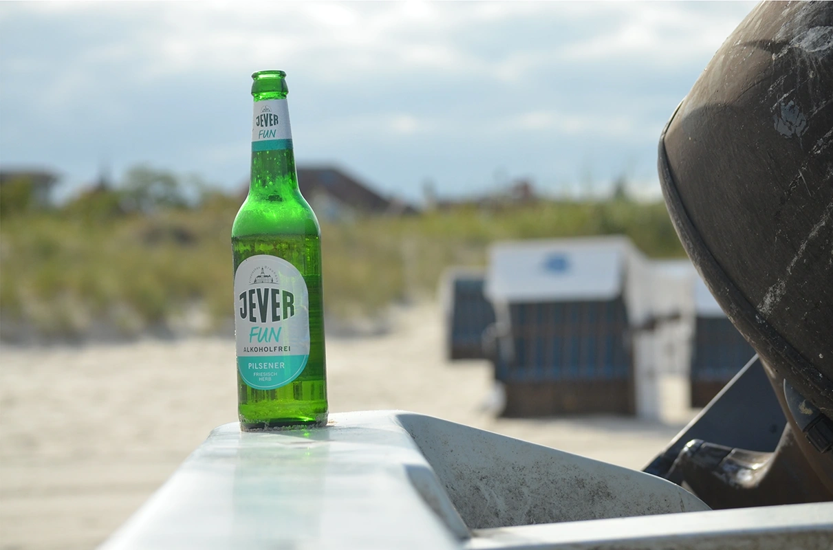 Jever Fun Alkoholfrei Flasche steht auf einer Metallplatte. Im Hintergrund Strandkörbe am Strand.