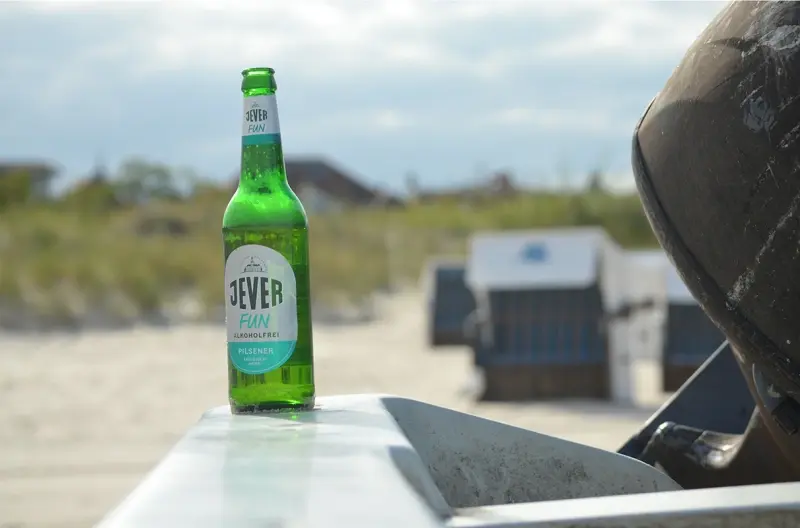 Jever Fun Alkoholfrei Flasche steht auf einer Metallplatte. Im Hintergrund Strandkörbe am Strand.