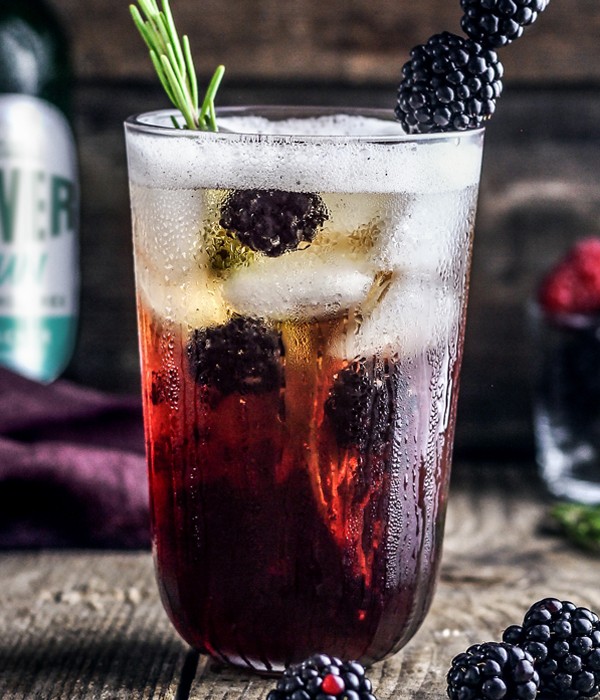 Ein kühles Getränk mit Brombeeren und Rosmarinzweig in einem hohen Glas.