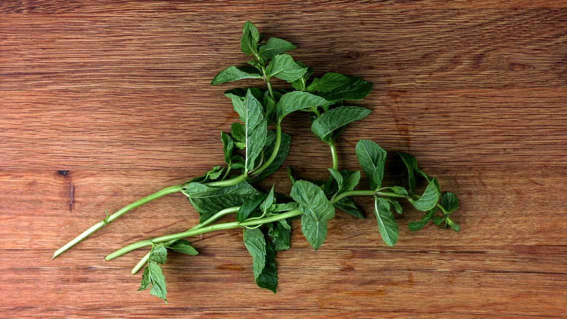 Frische grüne Minzblätter liegen locker verteilt auf einem Holzbrett.