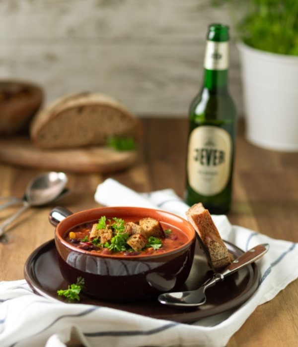 Eine Suppe in einer braunen Schüssel, garniert mit Kräutern, steht auf einem Teller neben Brot und einer Flasche.