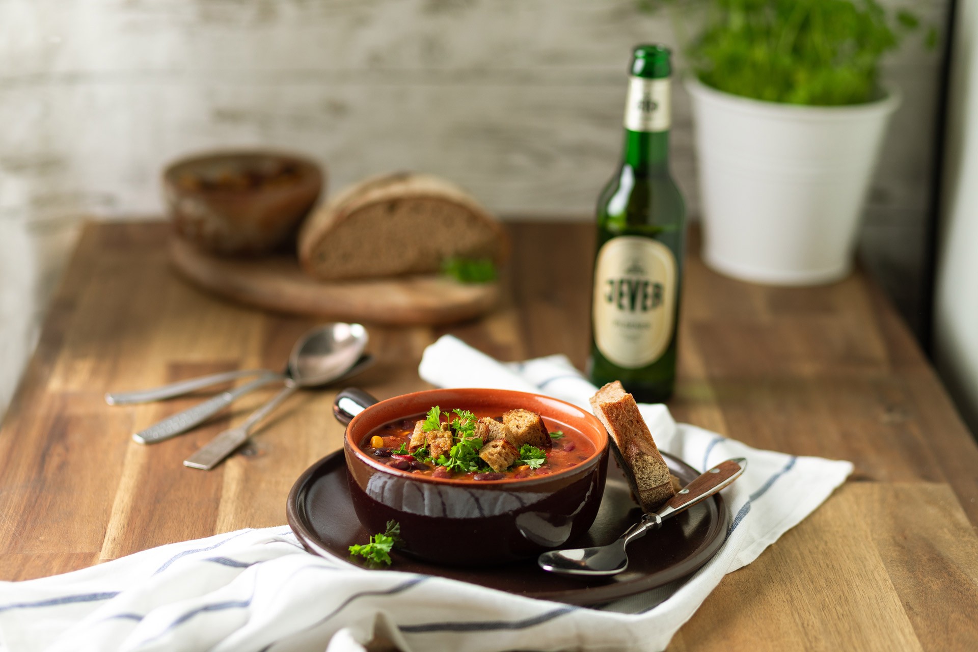 Eine Schüssel mit Suppe, garniert mit Kräutern und Croutons, steht neben einer Flasche auf einem Holztisch.