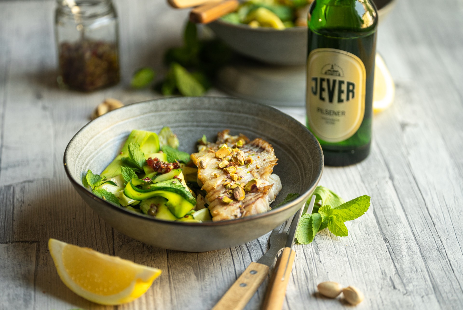 Eine Schüssel mit gebratenem Fisch und grünem Gemüse steht auf einem Holztisch.