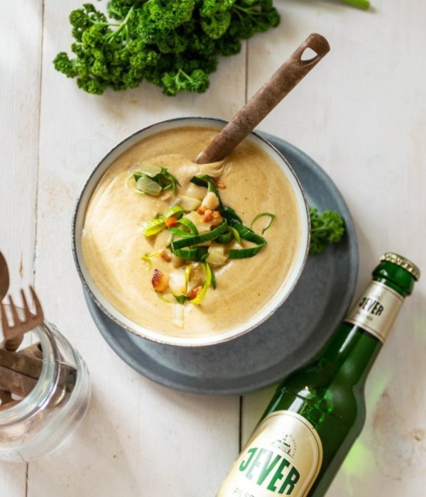Eine Schüssel mit cremiger Suppe ist garniert mit Gemüse und Kräutern, daneben steht ein grünes Getränk.
