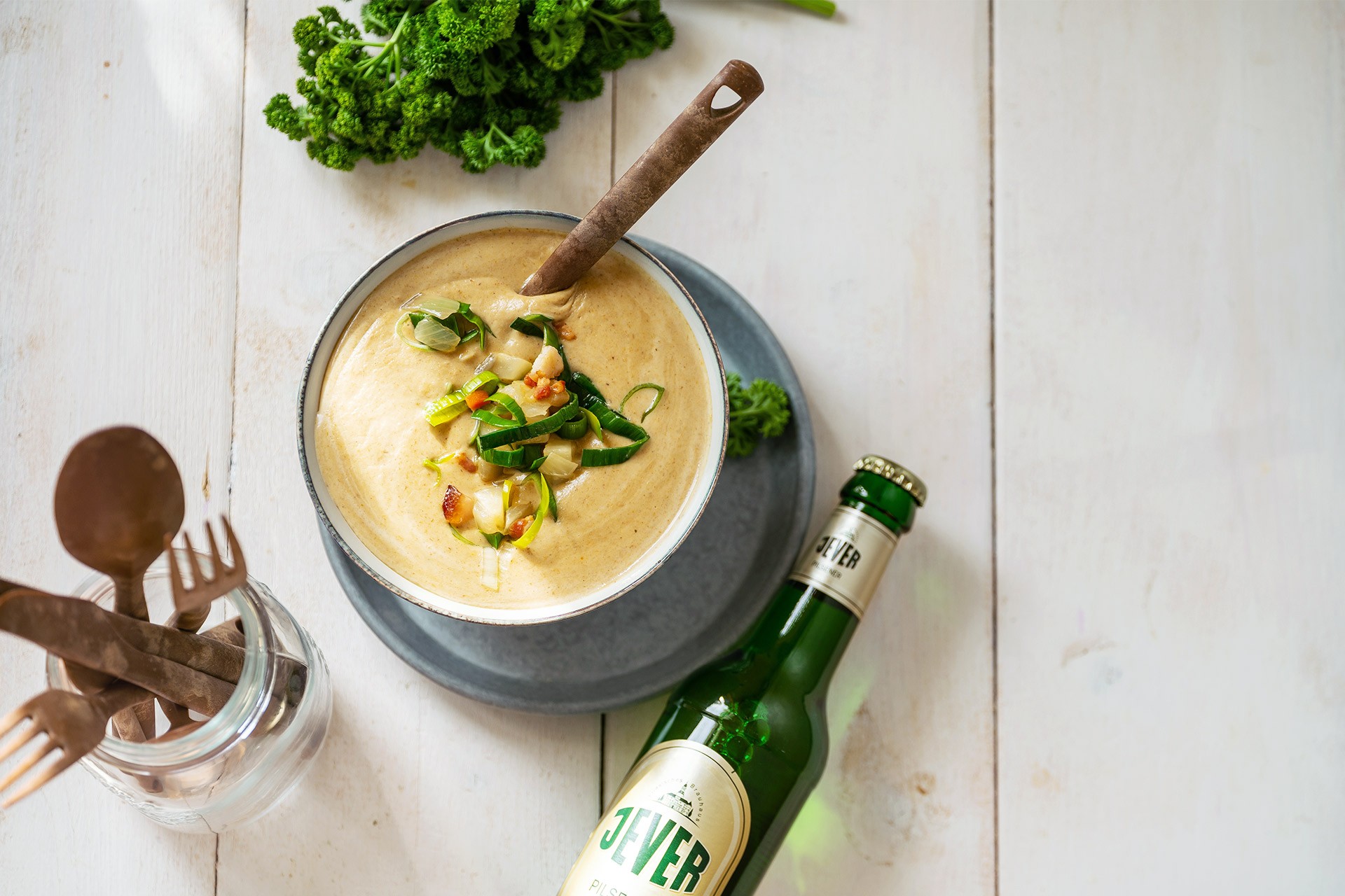 Ein Teller mit cremiger Suppe, garniert mit Gemüse, steht neben einer grünen Flasche auf einem Holztisch.